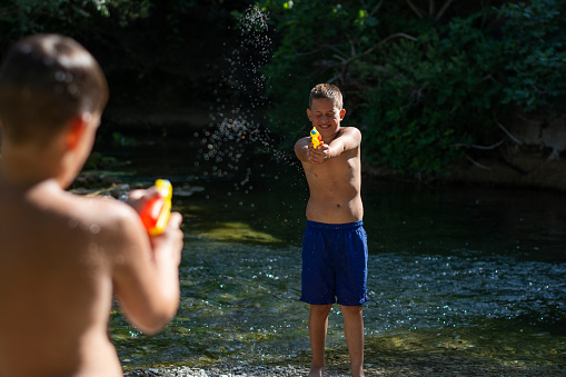 Two boys playing whit water guns in the river