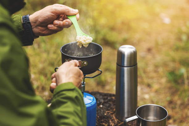 preparing oatmeal porridge outdoors on gas burner. camping cooking equipment stock photo