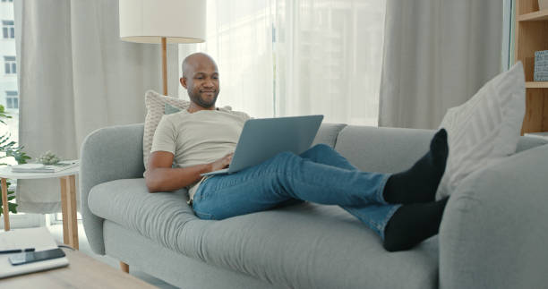 istock Shot of a young man using a laptop while sitting on the couch at home 1340709126