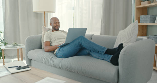 istock Shot of a young man using a laptop while sitting on the couch at home 1340709128