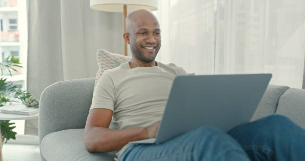istock Shot of a young man using a laptop while sitting on the couch at home 1340709134