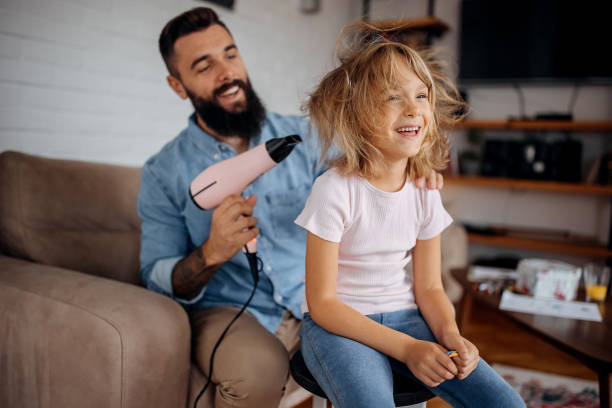Father drying his cute little daughter's hair with blowdryer stock photo