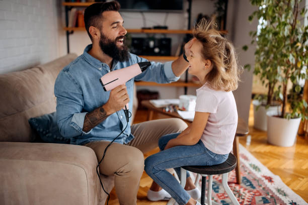 Young bearded single father drying his daughters hair in domestic room stock photo