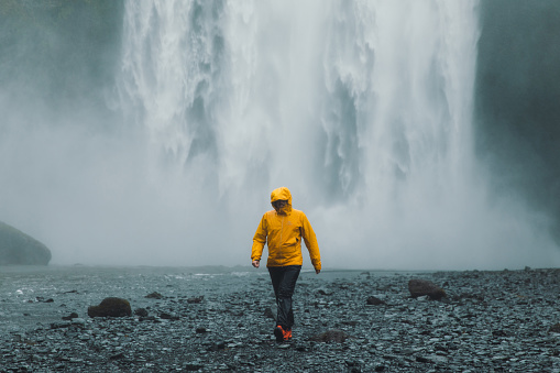 Silhouette of woman traveler in green jacket looking at the dramatic powerful Skogafoss waterfall in Iceland