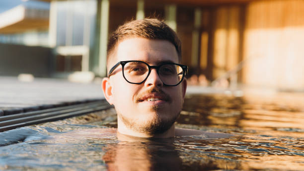 retrato de un hombre disfrutando de un baño en una piscina caliente durante la puesta de sol en islandia - baños térmicos fotografías e imágenes de stock