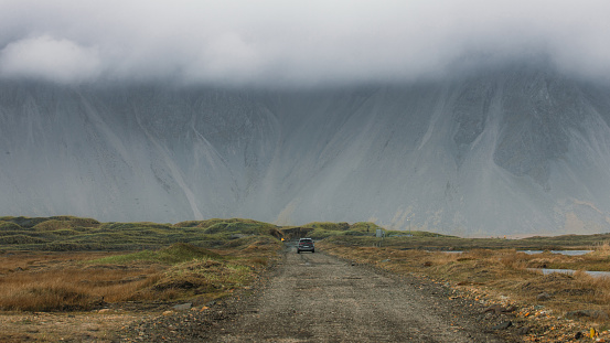 View of the car driving the scenic road with view of the panoramic wall mountain in clouds at East Fjords