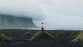 One woman traveler staying surrounded by the awe mountain landscape at the black sand dune beach in Iceland