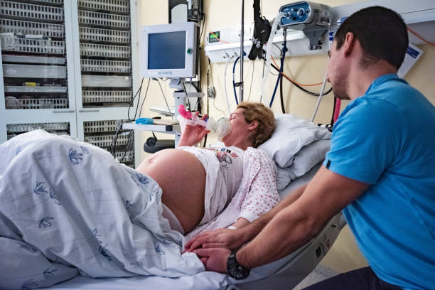 Woman is using laughing gas for labouring in delivery room and  holding husband's hand. stock photo