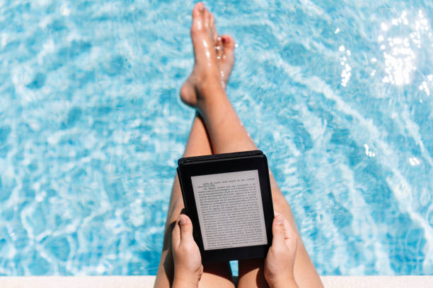 zrelaksowana dziewczyna czytająca e-booka na cyfrowym tablecie siedząc na półce basenu. - kindle e reader book reading zdjęcia i obrazy z banku zdjęć