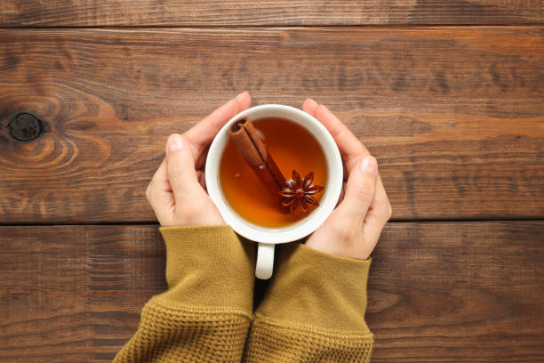 les mains tiennent une tasse de thé avec des épices, de l’anis et de la cannelle - anis photos et images de collection