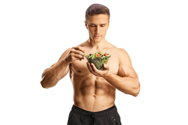 셔츠를 입지 않은 스포티한 남자가 서서 샐러드를 먹고 있습니다. - eating body building muscular build vegetable 뉴스 사진 이미지