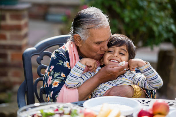 A Grandmothers Love Grandmother kissing her young grandsons face while sitting at a table in a garden in Middlesbourgh, North East of England. They are having al fresco lunch together. pakistani ethnicity stock pictures, royalty-free photos & images