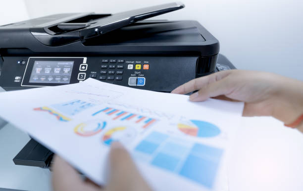 istock Office worker prints paper on multifunction laser printer. Copy, print, scan, and fax machine in office. Document and paper work. Print technology. Blurred hand hold printed paper. Scanner equipment. 1340721543