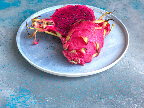 closeup halved tropical dragon fruit on the plate on blue background