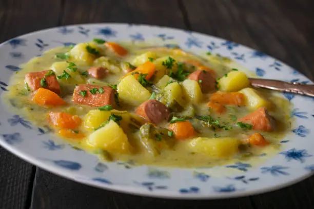 A plate or bowl with fresh cooked potato stew or soup served with vienna sausage on a rustic plate on wooden table. Closeup and isolated view with blurred background