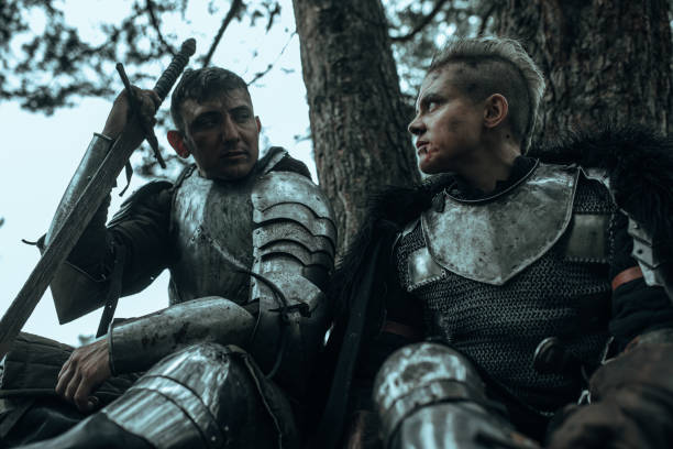 istock Two medieval knights in armour sit and rest among forest with sword. 1340723431