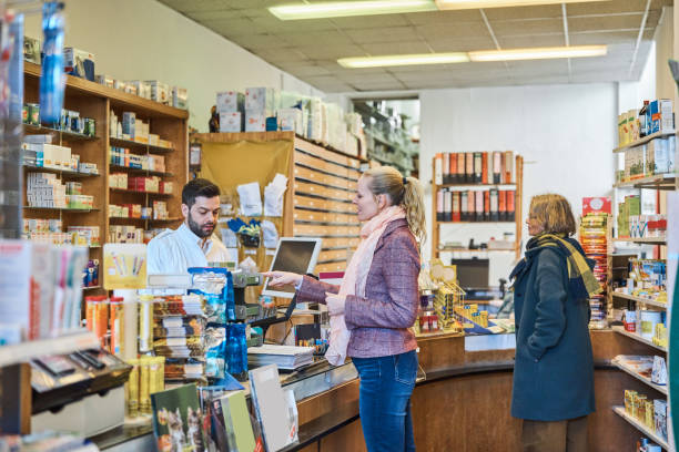 Female customer pointing while talking to cashier at pharmacy. Women are buying medicines at drug store. They are at checkout counter.