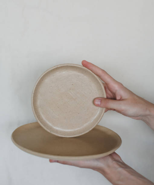 istock Hands holding ceramic plates isolated on white background. Minimalist set of handmade ceramic tableware and pottery 1340727709