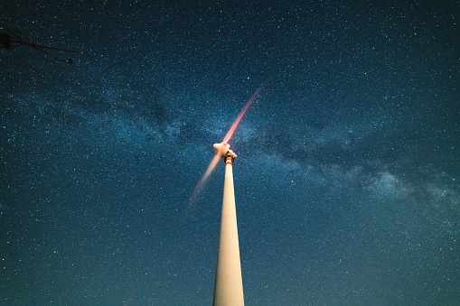 A wind turbine under the stars at night. Milky way in the background.