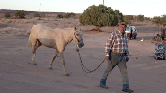 Mature Native American Navajo Man Walks a Horse in his front or back yard in Monument Valley Arizona or Utah at Dusk