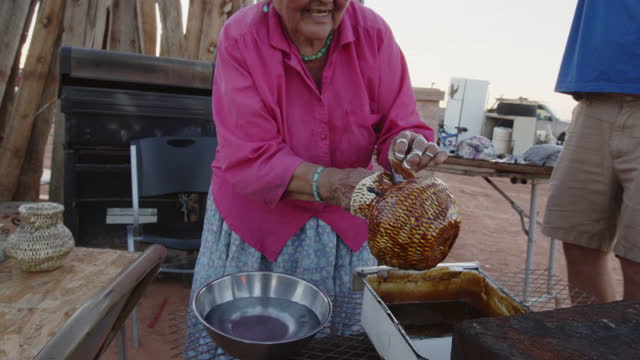 Elderly Navajo Woman Coating Her Newly Woven Baskets With Pitch, Heating On An Outdoor Wood Stove