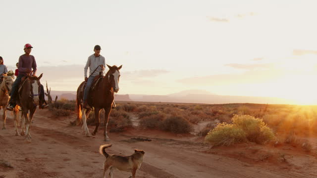 Slow Motion Teenage Native American Navajo Boys and Girls riding horses in the dramatic desert near Monument Valley Arizona or Utah under a dramatic sunset