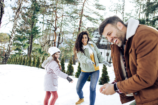 Happy family on winter vacation playing snowball fight.