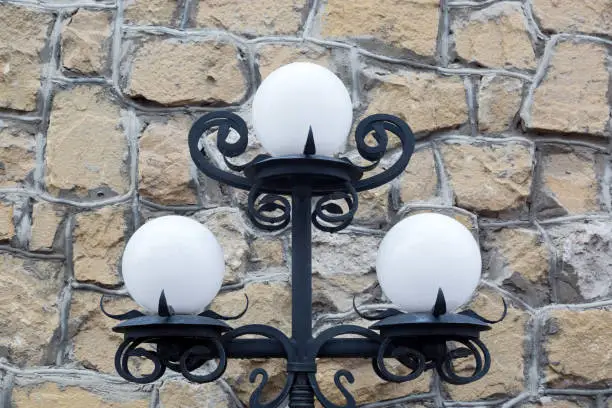 Beautiful black metal street lamp with three white balls on a gray stone background.