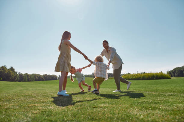istock Active young parents spending time together, holding hands in circle with their two little kids, boy and girl in green park on a summer day 1340733303
