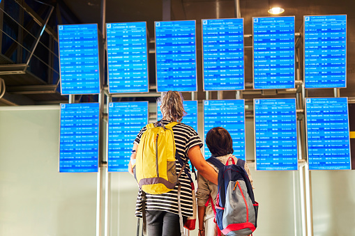 Passengers with backpack and suitcases looking at the departure board in the airport terminal