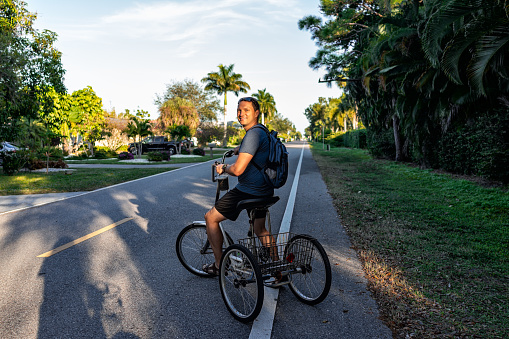 One young man standing riding tricycle bike with backpack on road at Naples park residential community district in Florida city