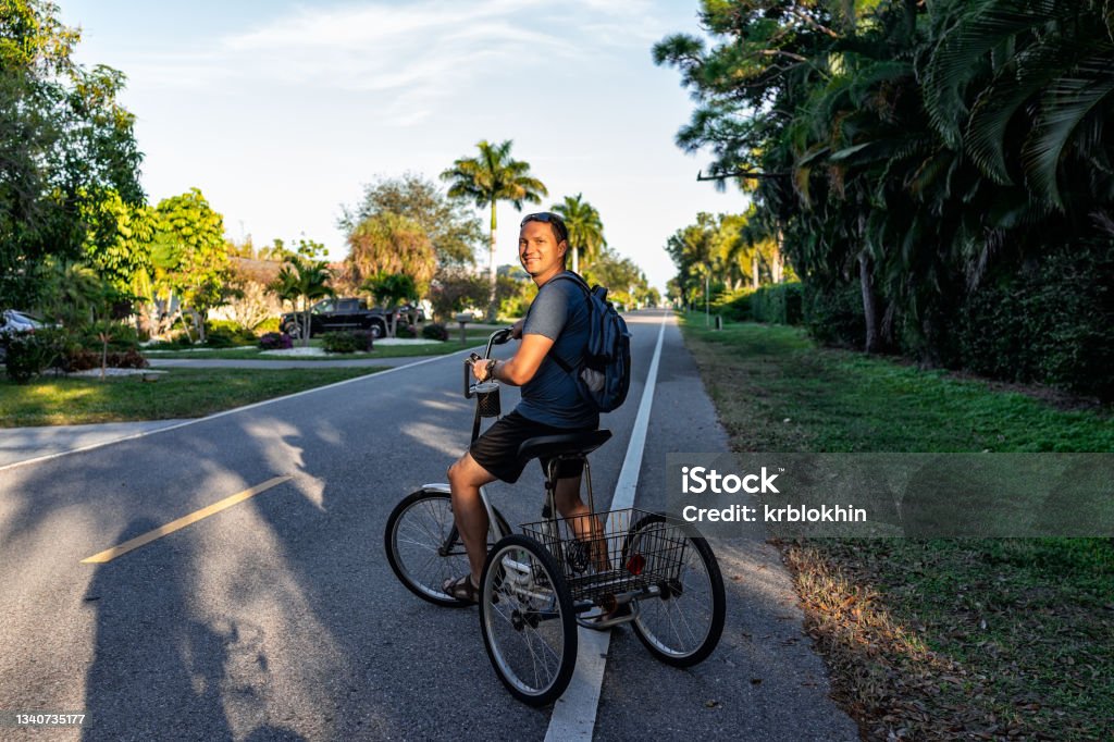 One young man standing riding tricycle bike with backpack on road at Naples park residential community district in Florida city Tricycle Stock Photo