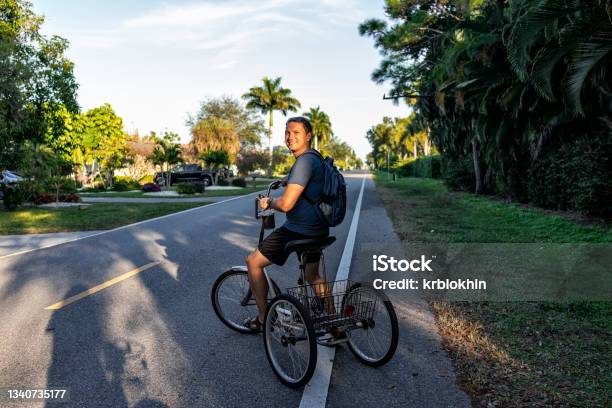 One Young Man Standing Riding Tricycle Bike With Backpack On Road At Naples Park Residential Community District In Florida City Stock Photo - Download Image Now