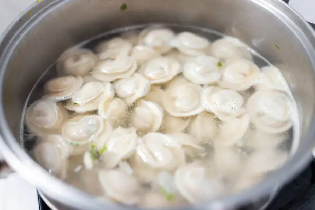 Closeup macro of stainless steel pot on stove top with traditional Russian dumplings pelmeni with meat steam cooking boiling