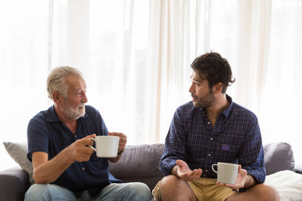 istock Senior father with adult son talking and drinking coffee while sitting on sofa at home with happy 1340738076