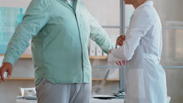 Doctor Measuring Waist of Overweight Man in Clinic