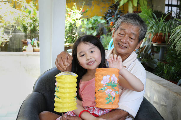 An Asian girl is feeling excited playing with vibrant colour lanterns with his grandpa at home.