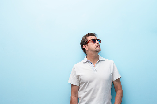 man in white casual clothes looking up next to blue wall