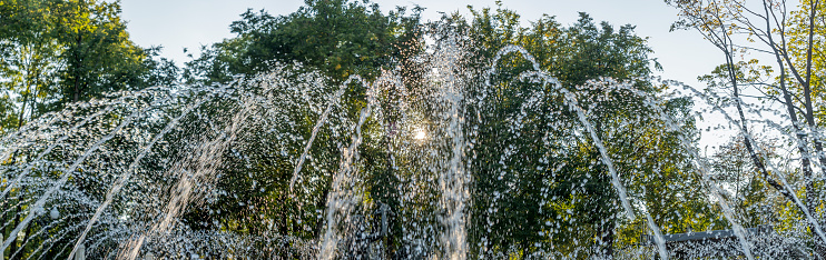 Splashing water in the fountain at summer city public urban park. Water jets abstract image close-up. Thin jets of pure clear aqua splashes flying upwards under pressure.