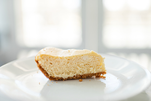 One piece slice of plain cheese cake cheesecake on plate at home or restaurant cafe isolated against blurry blurred white background