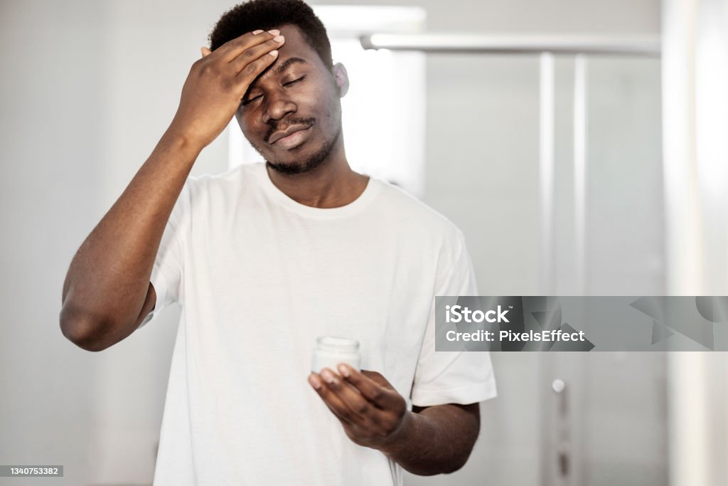 I make sure my skin is always in perfect condition African American Man Applying Facial Cream in the Bathroom Men Stock Photo