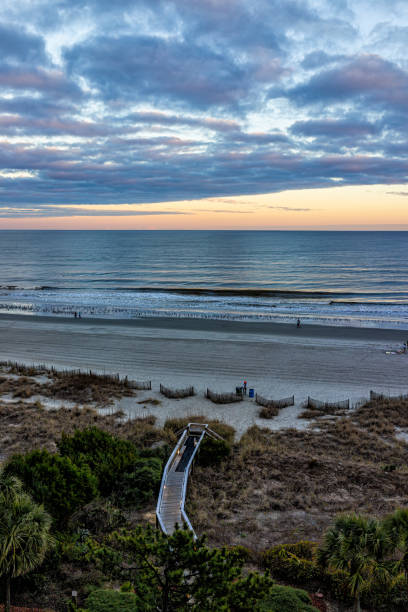 istock Myrtle Beach city with aerial high angle view overlook on Atlantic ocean at cloudy dramatic sunset with boardwalk beach access through sand dunes and sea oats plants to shore coast 1340753403