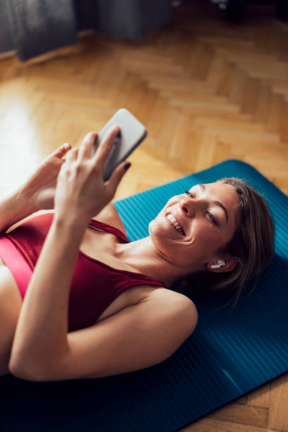 istock Smiling Woman With Wireless Earphones Lying On Exercise Mat and Using her Mobile Phone Before Workout 1340753577