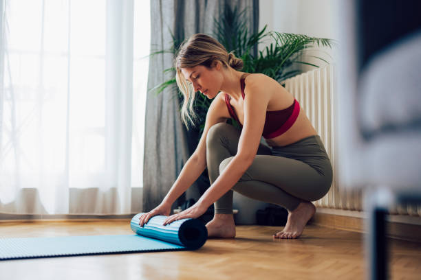 istock Happy Woman Folding Blue Exercise Mat on Wooden Floor 1340753623