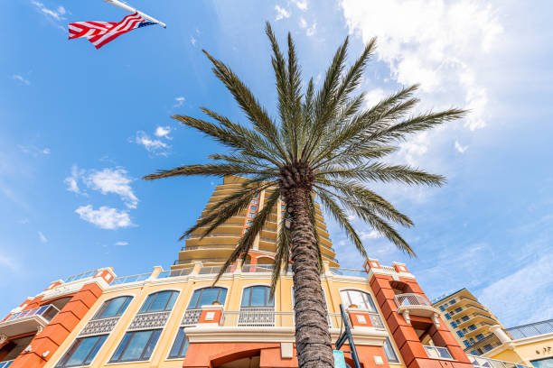 Looking up low angle view on shopping mall with American flag and store buildings architecture by Destin Harborwalk Village, Florida Panhandle with palm tree, blue sky Looking up low angle view on shopping mall with American flag and store buildings architecture by Destin Harborwalk Village, Florida Panhandle with palm tree, blue sky harborwalk stock pictures, royalty-free photos & images