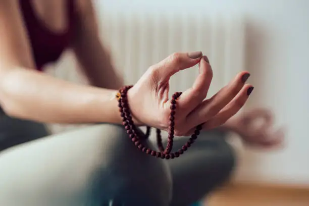 Close up of female sitting on floor and meditating while holding rosary beads in hand
