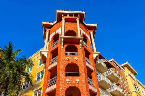 Colorful condos buildings with orange yellow colors corner, facade exterior with windows and palm tree by expensive luxury real estate property in Florida or Spain