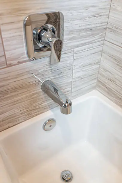 Closeup of new white modern tiled shower with bathtub bath tub with stainless steel faucet handles and drain hole at home house model staging showing