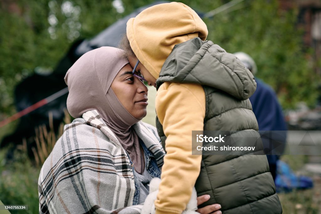 Family Reunification After Escape Happy middle-eastern mother in headscarf touching foreheads with daughter while finding her after escape from battlefield Refugee Stock Photo