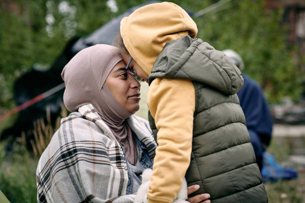 Family Reunification After Escape Happy middle-eastern mother in headscarf touching foreheads with daughter while finding her after escape from battlefield refugee camp stock pictures, royalty-free photos & images